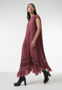 Robe maxi plissée en rose foncé, avec des accents rayés transparents, un ourlet volanté et des manches courtes. Portée avec des bottes à plateforme noires.