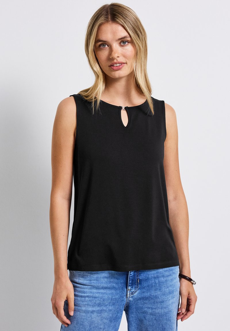 Musta ilmanhiha toppi, jossa on avainaukko yksityiskohta kauluksessa, valmistettu sileästä kankaasta. Yhdistettynä vaaleansinisiin farkkuihin.