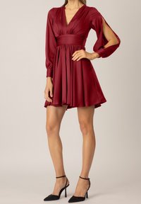 Röd satindress med V-ringning, långa puffärmar och skurna axlar. Utskuren kjol och åtsittande midja. Matchad med svarta spetsiga klackar.