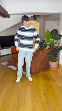 Prugasta pulover s belimi, sivimi in modrimi odtenki, izdelan iz pletenine. Usklajen s svetlobluščenimi hlačami in belimi športnimi čevlji.