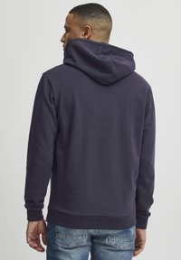 Granatowa bluza z kapturem o luźnym kroju, z kieszenią kangurką, ściągaczami przy mankietach i na hemie, wykonana z miękkiego materiału bawełnianego.