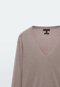 Pull en V en doux tissu tricoté mauve avec des manches longues et une texture subtile. Étiquette visible à l'intérieur de l'encolure, indiquant la marque et les informations d'entretien.
