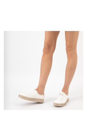 Nogi w białych sznurowanych tenisówkach z beżowymi plecionymi platformami na białym tle, jedna stopa lekko uniesiona.