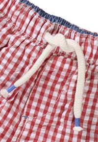 Pantalones cortos de cuadros rojos y blancos con una cinturilla elástica, que cuentan con un cordón blanco con un extremo azul. Textura de tela suave.