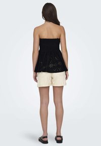 Haut smocké noir sans bretelles avec un design évasé à étages ; comportant des découpes en oeillet. Assorti avec un short cargo beige clair. Sandales noires.