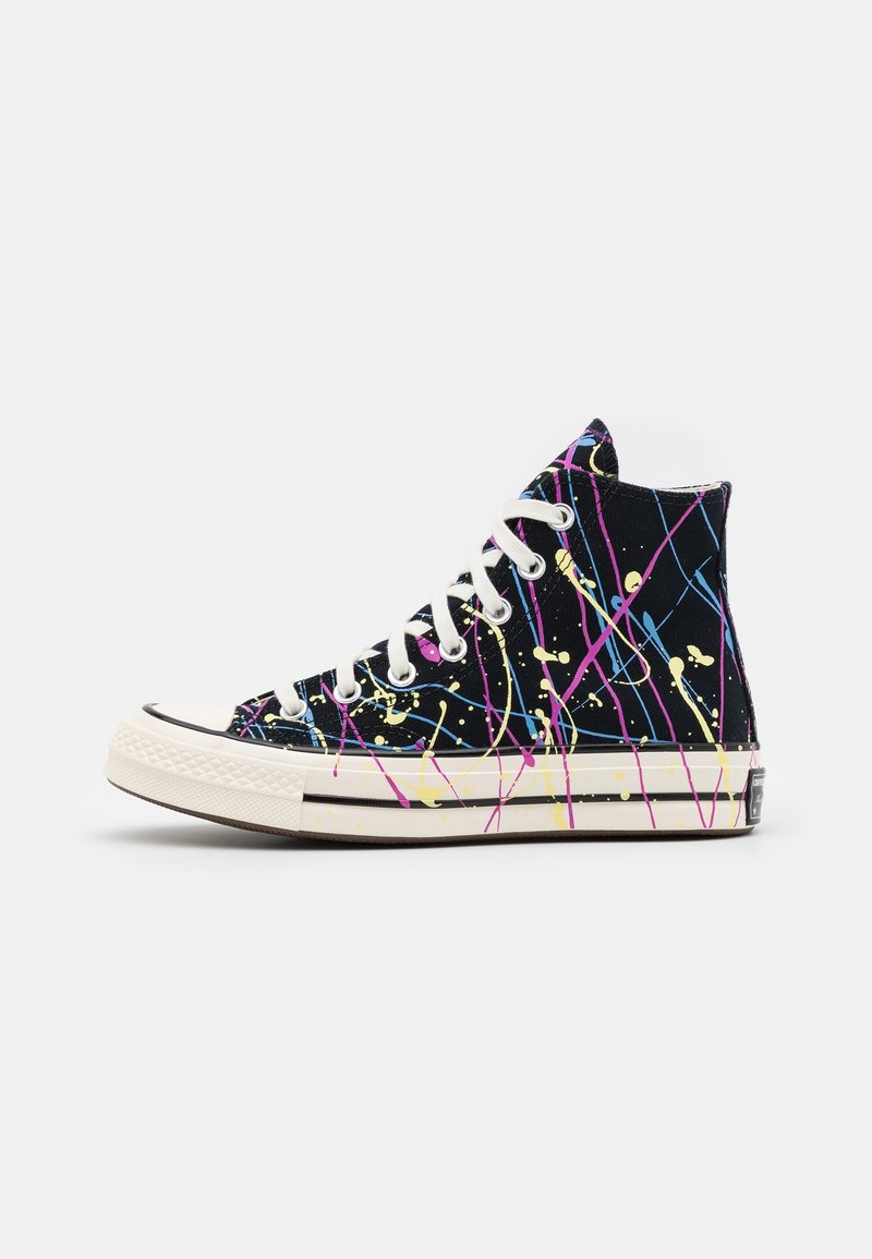 Basket montante noire avec semelle et lacets blancs, décorée de projections de peinture colorée en rose, jaune et bleu sous forme de lignes et de points.
