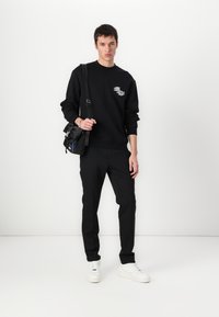 Sweatshirt preto com gráfico branco, calças pretas ajustadas e ténis brancos. Os acessórios incluem uma mala tiracolo preta.