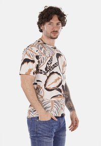Camisa de manga corta en crema con un gran estampado de hojas en marrón y negro. Presenta un cuello redondo y un ajuste relajado.