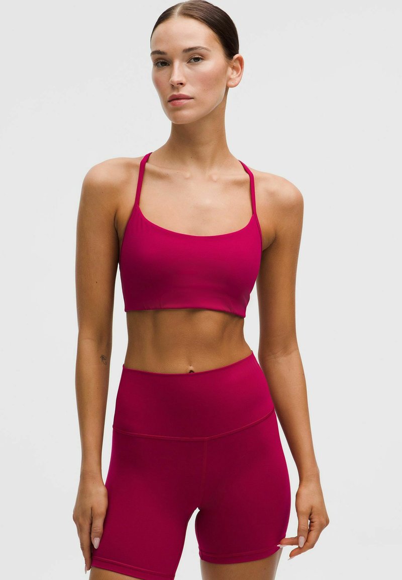 Fuchsiová športová podprsenka s tenkými ramienkami, skombinovaná s vysokými šortkami, oboje vyrobené z hladkého, pružného materiálu, s bezšvovým dizajnom.