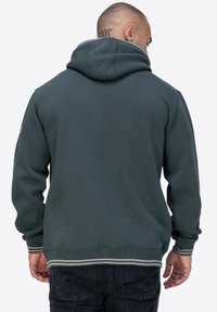Sudadera con capucha de color verde oscuro que presenta puños y dobladillo acanalados con rayas grises, hecha de tela suave, mostrando un diseño simple sin logotipos.