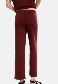 Bordowe dzianinowe spodnie o prostym kroju. Miękka tekstura, elastyczny pas i brak widocznych zapięć lub kieszeni.