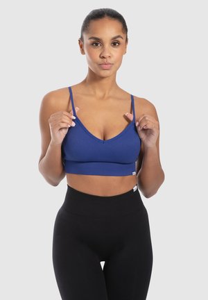 Blauwe geribbelde crop top met verstelbare dunne bandjes. Heeft een diepe V-halslijn en een aansluitende silhoutte. Gecombineerd met hoge zwarte leggings.