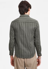 Camicia da uomo a maniche lunghe di colore verde scuro con strisce verticali bianche, dotata di colletto, polsini con bottoni e orlo arrotondato sul retro.