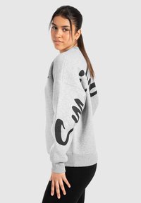 Sweatshirt gris oversize avec texte graphique noir sur la manche, manches et ourlet côtelés. Fabriqué en matière polaire douce.