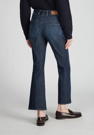 Jeans acampanados de mezclilla oscura con cintura de altura media, que presentan dos bolsillos traseros y detalles de cuero marrón en la cinturilla.