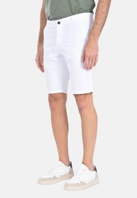 Pantaloni corti bianchi casual realizzati in tessuto leggero, dotati di chiusura con bottone, tasche laterali e orlo arrotolato, abbinati a sneaker bianche.