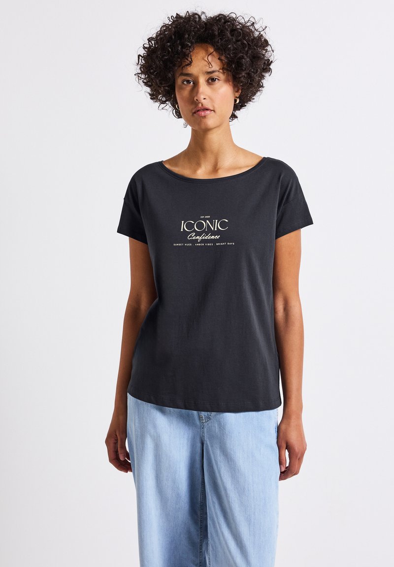 Černé bavlněné tričko s krátkými rukávy a kulatým výstřihem. Na přední straně je v bílém písmu nápis "ICONIC Confidence". Kombinováno se světlemodrými džíny.