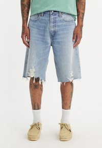 Blå denimshorts med fransade kanter och slitage. Har en avslappnad passform, kontrasterande sömmar och fem fickor.