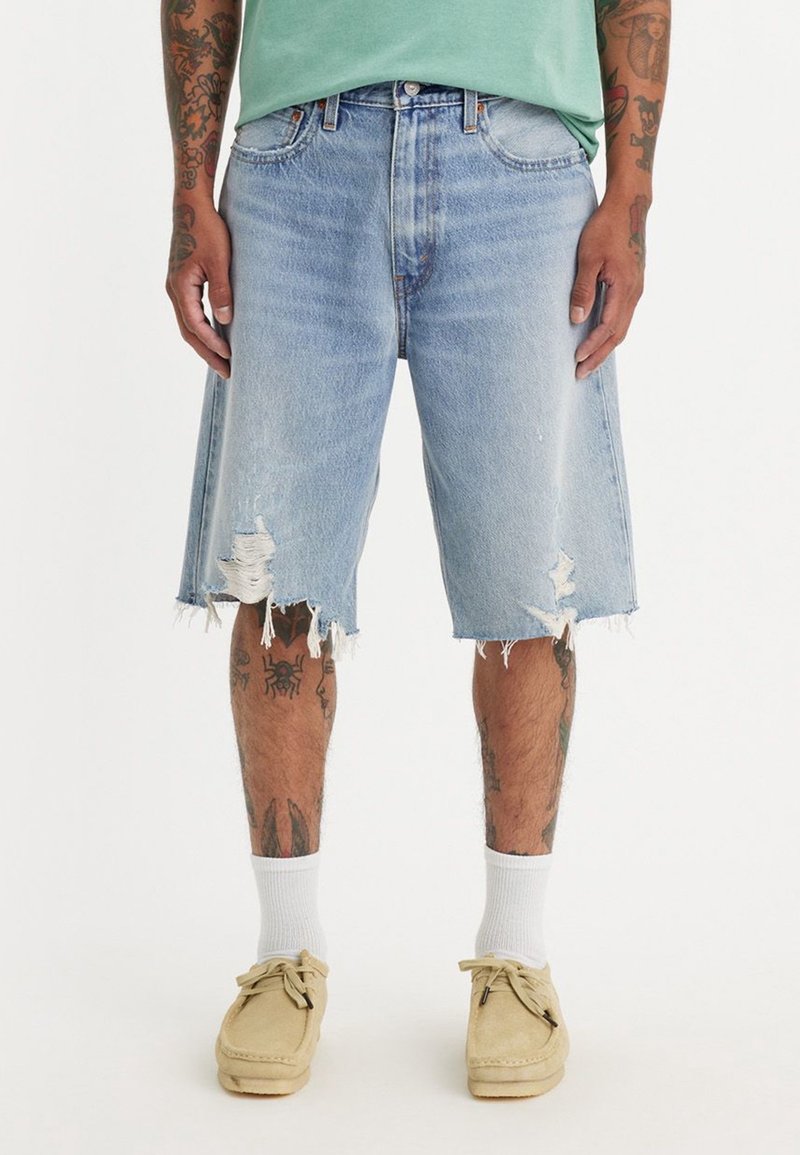 Blå denimshorts med fransade kanter och slitage. Har en avslappnad passform, kontrasterande sömmar och fem fickor.