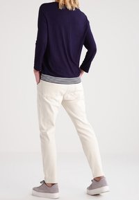 Navy longsleeve top met gestreepte zoom, gecombineerd met lichtgekleurde tapered broek en grijze sneakers; zachte stof en relaxte pasvorm.