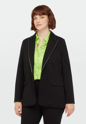 Zwarte blazer met een contrasterende zwarte revers, gecombineerd met een heldergroene knoopshirt. Bevat twee voorzakken en heeft een ontspannen pasvorm.