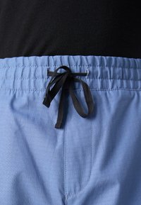 Calções de banho azul-claro com um padrão texturizado, apresentando um cordão preto na cintura e um acabamento de tecido suave.