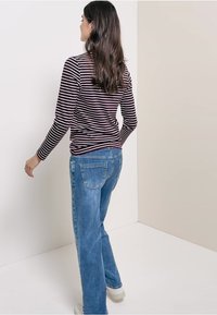 Long-sleeve, burgundy and white striped top paired with light blue straight-leg jeans and white sneakers, viewed from the back.