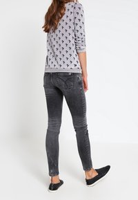 Felpa grigia con un motivo di piccoli alberi neri, abbinata a jeans skinny neri sbiaditi e scarpe slip-on nere. Vista posteriore.