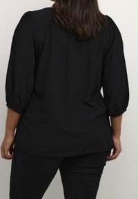 Blusa nera a coste con maniche a sbuffo a tre quarti e scollatura rotonda, caratterizzata da una vestibilità comoda e un tessuto liscio.
