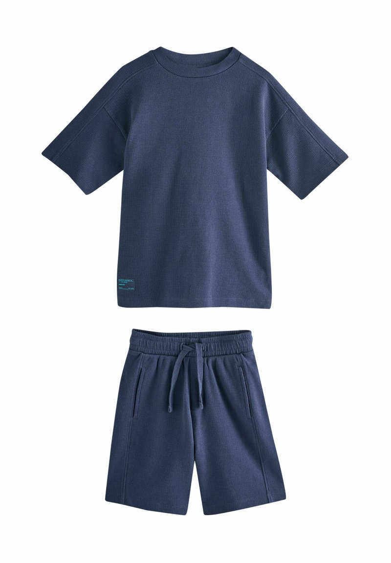 Maglietta in misto cotone blu navy con trama a coste e scollo tondo, abbinata a pantaloncini coordinati a coste con vita elasticizzata e tasche.