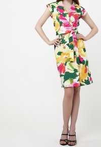 Kukallinen kietaisumekko kirkkaissa väreissä (vaaleanpunainen, keltainen, vihreä) jossa on lyhyet hihat, solmittava vyötärö ja nappiyksityiskohtia. Sileä kangas elävällä kuviolla.