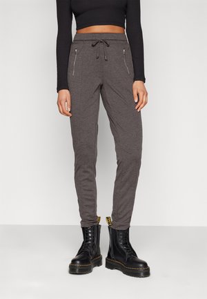 Pantalon de jogging gris avec une taille à cordon, poches zippées et une coupe effilée. Associé à des bottes noires à lacets. Texture de tissu lisse.