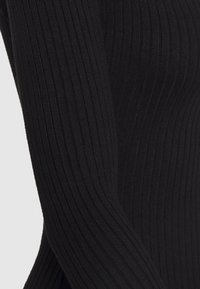 Haut noir à manches longues côtelé avec un tissu texturé à rayures verticales, conçu pour une silhouette ajustée.