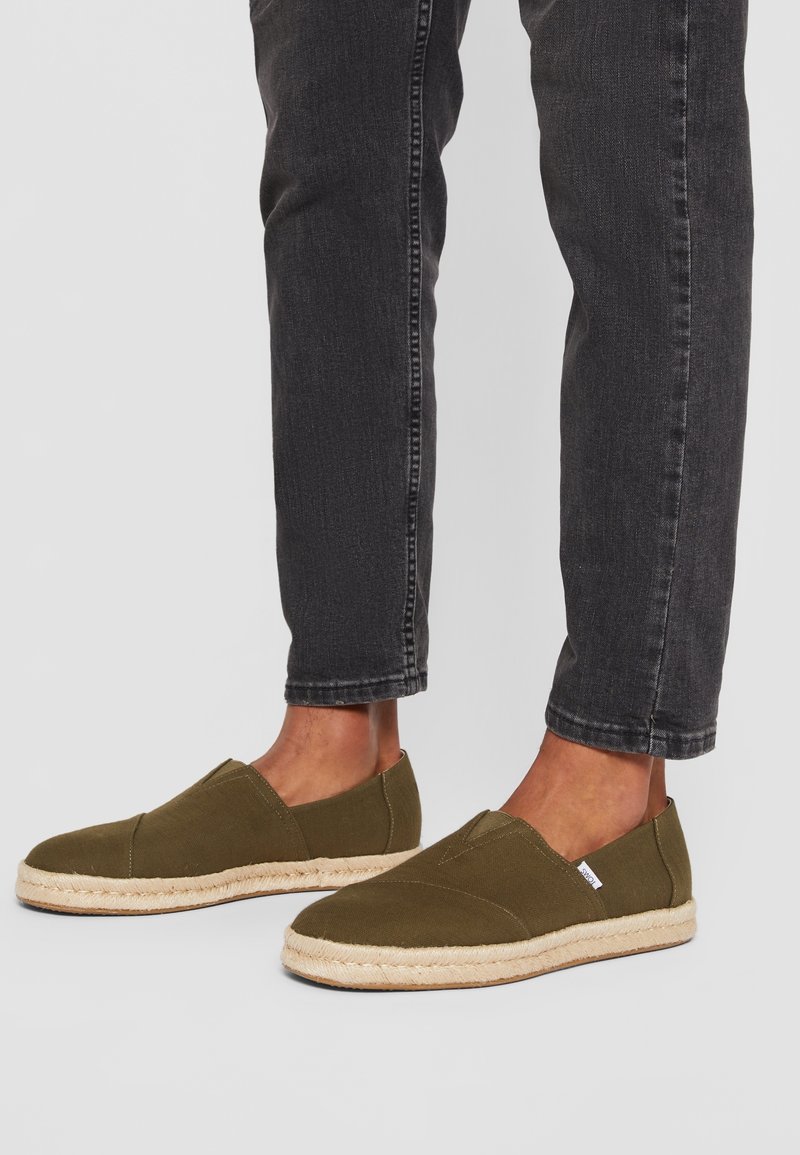 Chaussures espadrilles vert olive à enfiler, tige en tissu et semelle en corde de jute, associées à un jean slim foncé.