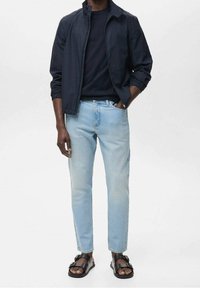 Laivaston kevyt takki, musta pyöreäkauluksinen t-paita, vaaleansiniset farkut ja mustat sandaalit solkikoristein. Rentoon tyyliin sopiva, jämäkkä istuvuus.