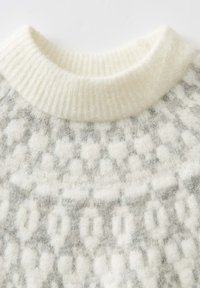 Maglione grigio chiaro e bianco con motivo, dotato di un collo a coste di colore bianco crema. Realizzato in un tessuto morbido e testurizzato con un aspetto peloso.