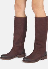 Botas de cuero marrón hasta la rodilla con un acabado texturizado, punta redondeada y tacón apilado. Presentan un detalle de punta de contraste lisa.