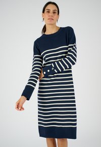Abito a righe blu navy in tessuto morbido; presenta righe orizzontali bianche e polsini abbottonati, con scollatura rotonda e vestibilità ampia.