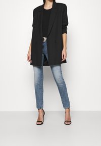 Black double-breasted blazer over a black top, paired with light blue skinny jeans and black strappy heels. Clean lines and minimal design.