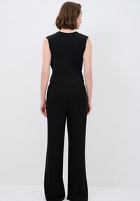 Schwarzes ärmelloses Top mit taillierter Passform, kombiniert mit weiten schwarzen Hosen. Glatte Textur, minimalistisches Design und keine sichtbaren Hardware-Details.
