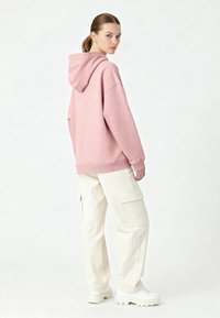Sweat à capuche oversize rose avec cordon de serrage, ourlet et poignets côtelés, associé à un pantalon cargo crème clair et des baskets blanches épaisses.