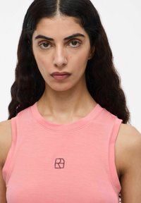Rosa linne utan ärmar gjort av mjukt tyg, med en subtil broderad logotyp över bröstet. Urdning är rund och välsittande.