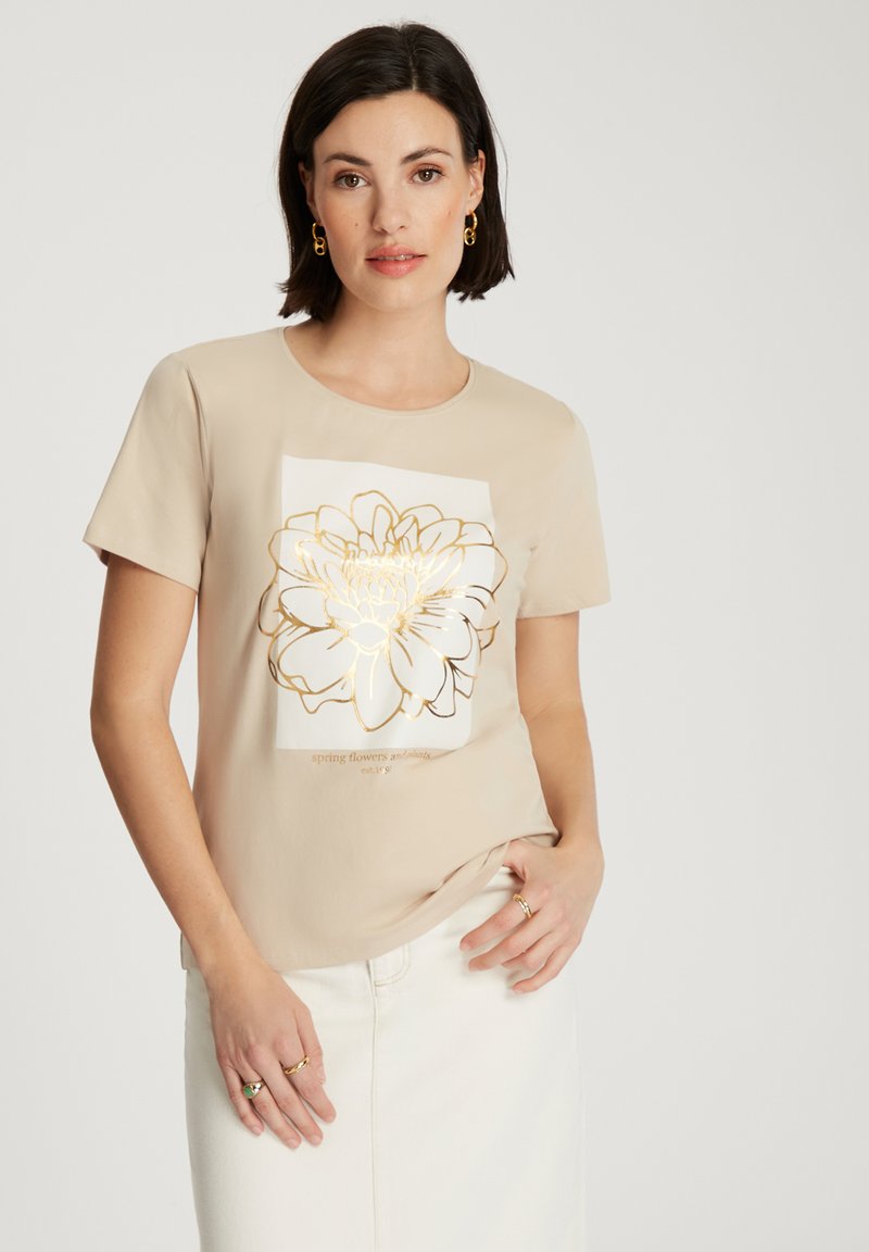 Beżowa koszulka z krótkim rękawem z białym prostokątnym nadrukiem kwiatowym obramowanym złotem. Miękka tkanina o luźnym kroju. Minimalistyczny design.