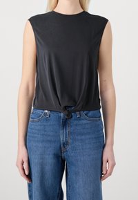 Top nero senza maniche con dettaglio anteriore annodato, realizzato in un materiale morbido. Abbinato a jeans in denim blu a vita alta.