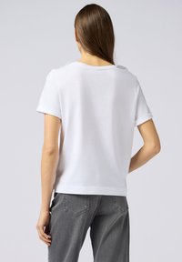 Witte katoenen t-shirt met korte opgerolde mouwen, ronde halslijn en een gewone pasvorm. Draagt bij grijze denim broek, met een eenvoudige, schone uitstraling.