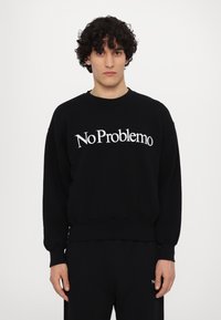 Sudadera negra de algodón con mangas largas, puños y cinturilla acanalados. Presenta el texto blanco "No Problemo" en la parte frontal.