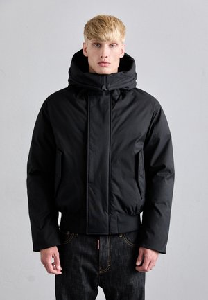 Schwarze, mit Kapuze versehene Steppjacke mit Reißverschluss vorne, elastischen Bündchen und Seitentaschen. Glatte Textur, cropped Länge und minimalistisches Design.