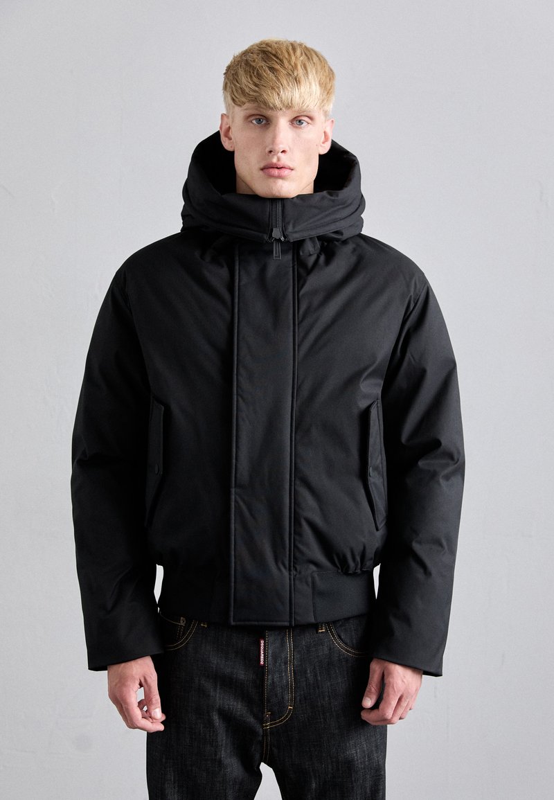 Black hooded puffer jacket with a zipped front, elastic cuffs, and side pockets. Smooth texture, cropped length, and minimalistic design.