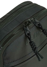 Bolsa negra de nylon con doble cremallera y acabado texturizado. Presenta un logo, un tirador decorativo de cordón y costuras reforzadas para mayor durabilidad.