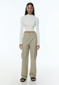 Crème ribbed cropped top met lange mouwen, gecombineerd met lichtkhaki cargobroek met zijzakken en een ontspannen pasvorm. Zwarte sandalen maken de look compleet.